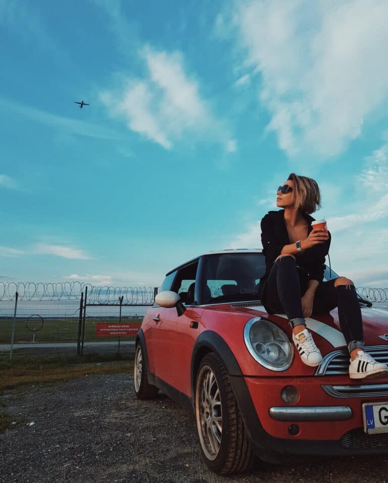 woman sitting on hood of car with coffee watching airplanes